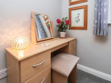 A wooden dressing table with a mirror, lamp, flower pot, and a cushioned stool at Esk Retreat in Whitby