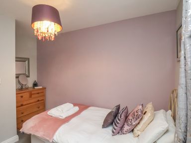 A bedroom with a bed with pillows and a folded towel on a blanket a wooden dresser with a mirror and a lamp hanging from the ceiling at Esk Retreat in Whitby