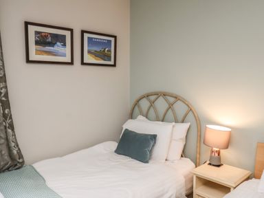 A bedroom with a single bed with white bedding a teal pillow and a bedside table with a lamp and two framed pictures on the wall at Esk Retreat in Whitby