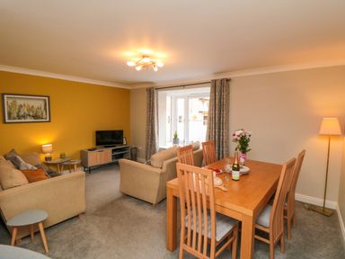 A living and dining room with beige sofas, a wooden dining table with chairs, and a television on a stand at Esk Retreat in Whitby