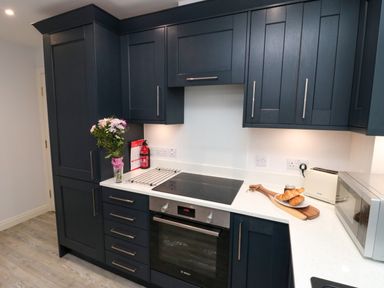 A kitchen with dark cabinets a vase of flowers a stovetop oven croissants on a cutting board a toaster and a microwave at Esk Retreat Whitby