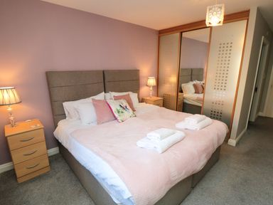 A bedroom with a double bed two bedside tables with lamps and mirrored sliding wardrobe doors at Esk Retreat in Whitby