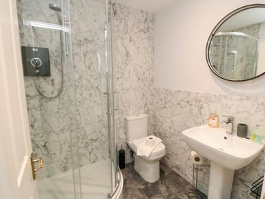 A bathroom with a glass shower enclosure a toilet and a pedestal sink with a round mirror at Esk Retreat in Whitby