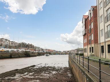 A river with boats docked along the banks and buildings on the right side at Esk Retreat in Whitby