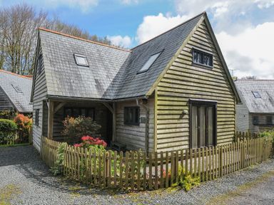 An exterior view of a wooden house with a fenced garden and gravel driveway at Stow Cottage in Davidstow near Camelford