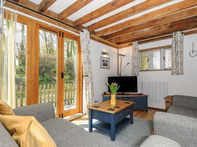 A sitting room with wooden beams grey sofas a blue coffee table and a television at Stow Cottage in Davidstow near Camelford