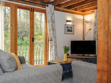 A living room with gray sofas a wooden coffee table a flat screen tv and large wooden framed glass doors at Stow Cottage in Davidstow near Camelford