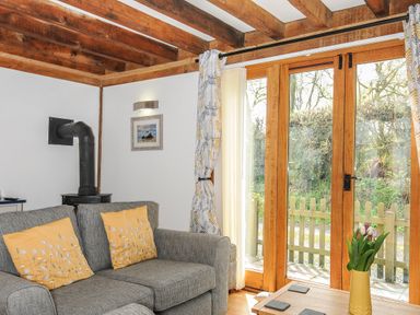 A living room with a gray sofa with yellow pillows a wood burner and glass doors opening to a garden at Stow Cottage in Davidstow near Camelford