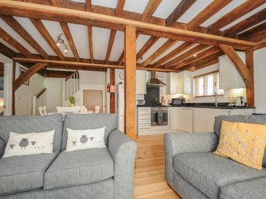 A living room with two grey sofas and a kitchen with white cabinets and wooden beams at Stow Cottage in Davidstow near Camelford