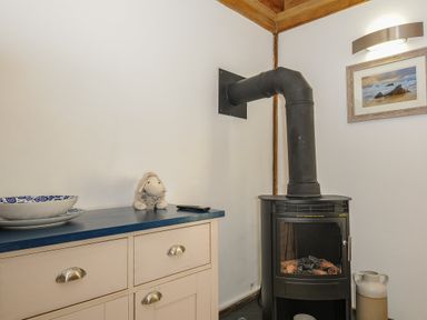 A stove with a black chimney pipe next to a cabinet with drawers and a framed picture on the wall at Stow Cottage in Davidstow near Camelford