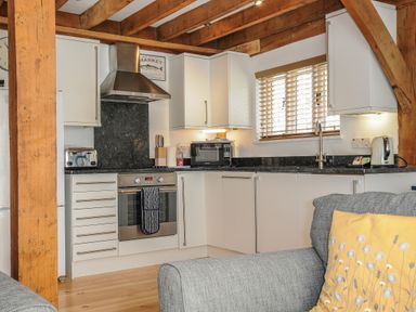 A kitchen with white cabinets wooden beams a grey sofa with a yellow pillow at Stow Cottage in Davidstow near Camelford