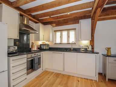 A kitchen with white cabinets wooden beams a window toaster kettle and oven at Stow Cottage in Davidstow near Camelford
