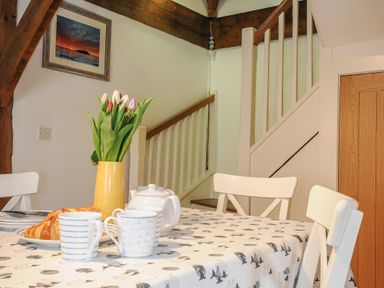 A dining table with cups a teapot croissants and tulips near a staircase at Stow Cottage in Davidstow near Camelford