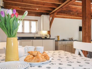 A kitchen with a wooden beam ceiling and a table set with croissants flowers and cups at Stow Cottage Davidstow near Camelford