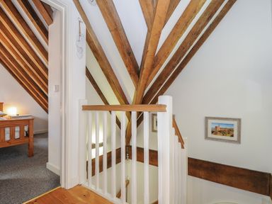 A staircase landing with wooden beams and a view into a bedroom at Stow Cottage in Davidstow near Camelford