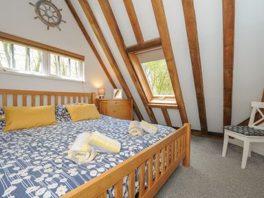 A bedroom with wooden bed blue and white bedding yellow pillows wooden window frame dresser chair and sloped ceiling at Stow Cottage in Davidstow near Camelford
