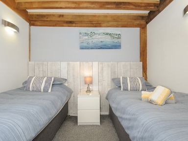 A bedroom with two single beds a white nightstand and a painting on the wall at Stow Cottage in Davidstow near Camelford