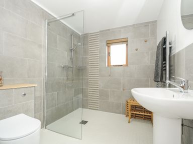 A bathroom with a walk-in shower toilet pedestal sink towel rack and wooden stool at Stow Cottage in Davidstow near Camelford
