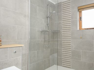 A bathroom shower area with grey tiled walls a glass shower screen and a small window at Stow Cottage in Davidstow near Camelford