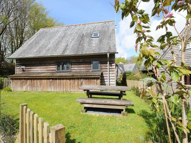A wooden house with a sloped roof and a grassy yard with 2 picnic tables at Stow Cottage in Davidstow near Camelford