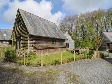 A wooden cottage with a fenced garden and picnic table surrounded by trees at Stow Cottage in Davidstow near Camelford