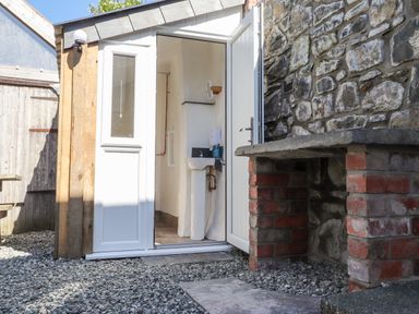 An outdoor area with a white door open revealing a small sink inside and a stone and brick structure beside it at Morawel Newport Pembrokeshire