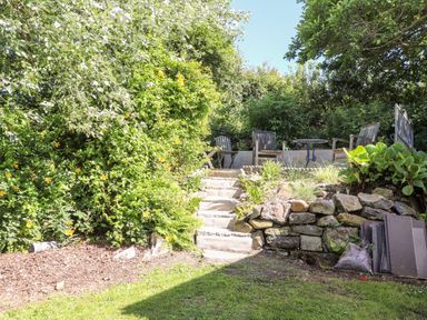 A garden area with stone steps leading to wooden chairs and a small round table at Morawel in Newport Pembrokeshire