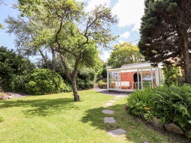 A garden with a tree a path of stepping stones and a glass enclosed seating area at Morawel in Newport Pembrokeshire