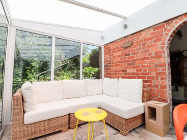 A conservatory with a wicker corner sofa with white cushions a yellow round table and a wooden side table at Morawel Newport Pembrokeshire