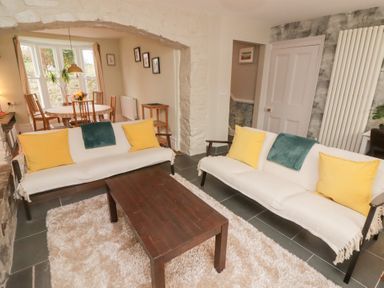 A living room with two sofas with yellow pillows and a wooden coffee table next to a dining area with a round table and chairs at Morawel in Newport Pembrokeshire
