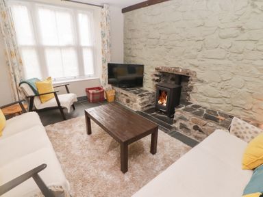 A living room with a stone wall fireplace wood stove sofas armchair wooden coffee table and large window at Morawel in Newport Pembrokeshire
