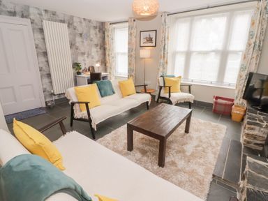 A living room with sofas yellow cushions a coffee table a desk and a TV at Morawel Newport Pembrokeshire