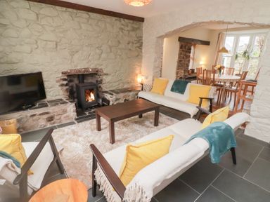 A living room with sofas yellow cushions and a wood stove visible through an archway at Morawel in Newport Pembrokeshire