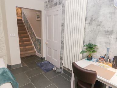 A hallway with stairs carpeted in beige and floral wallpaper a white door a tall white radiator a desk with office supplies and a plant and a brown chair at Morawel Newport Pembrokeshire