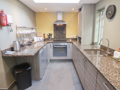 A kitchen with granite countertops a stove a sink and hanging mugs at Morawel in Newport Pembrokeshire