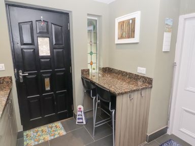 A kitchen corner with a black door a granite countertop with two black chairs and a small window with stained glass at Morawel Newport Pembrokeshire
