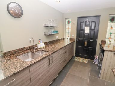 A kitchen with granite countertops a double sink glasses on shelves a black door and tiled floor at Morawel Newport Pembrokeshire