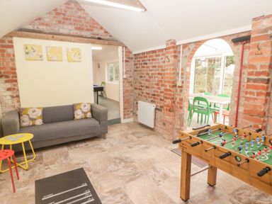 A room with exposed brick walls a gray sofa a foosball table and yellow and red stools at Morawel Newport Pembrokeshire