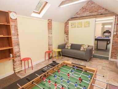 A game room with a foosball table two red stools a yellow side table a gray couch and a pool table in a connected room at Morawel Newport Pembrokeshire