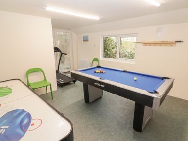 A game room with a pool table blue felt an air hockey table a treadmill and green chairs at Morawel in Newport Pembrokeshire