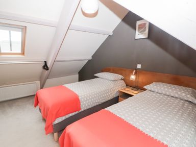 A bedroom with two single beds side by side with patterned bedding and coral blankets at Morawel in Newport Pembrokeshire
