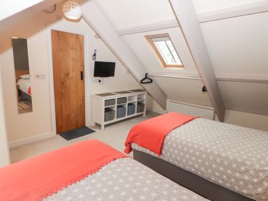 A bedroom with two single beds a wooden door a small wall mounted TV a white storage unit and a skylight at Morawel Newport Pembrokeshire