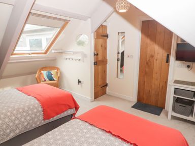 A bedroom with two beds covered with patterned bedding and red throws a wicker chair under a skylight window and two wooden doors at Morawel Newport Pembrokeshire