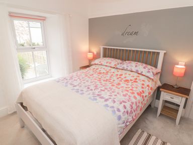 A bedroom with a bed with patterned bedding bedside tables lamps and a window at Morawel Newport Pembrokeshire