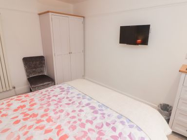 A bedroom with a bed covered with a multicolored leaf pattern duvet a white wardrobe a dark grey chair a wall-mounted TV and a white cabinet at Morawel in Newport Pembrokeshire