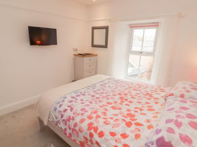 A bedroom with a bed covered in patterned bedding a small chest of drawers a wall-mounted television and a window at Morawel Newport Pembrokeshire
