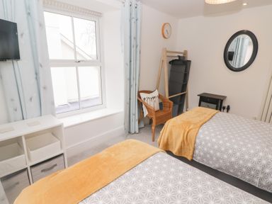 A bedroom with two single beds with blankets a wicker chair with cushions and a shelving unit at Morawel in Newport Pembrokeshire