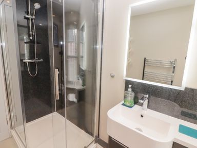 A bathroom with a glass shower enclosure a sink with a faucet and a lit mirror at Morawel in Newport Pembrokeshire