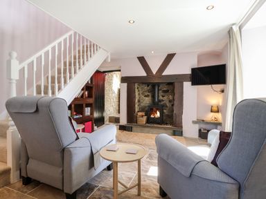 A sitting room with armchairs a wood burning stove and a staircase at Morawel Fach in Newport Pembrokeshire