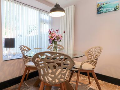 A dining area with a round glass table surrounded by four patterned chairs and a vase of flowers on the table at Morawel Fach in Newport Pembrokeshire